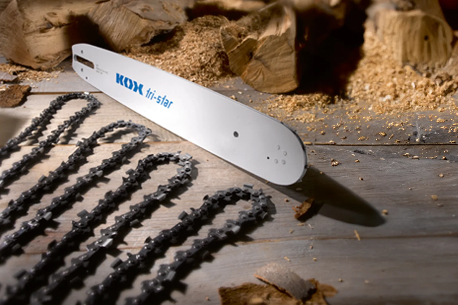 Eine Motors�genschiene mit der Aufschrift „KOX tri-star“ liegt auf einer Holzfl�che. Daneben sind mehrere Motors�genketten ordentlich ausgelegt, im Hintergrund befinden sich Holzst�cke und S�gesp�ne.