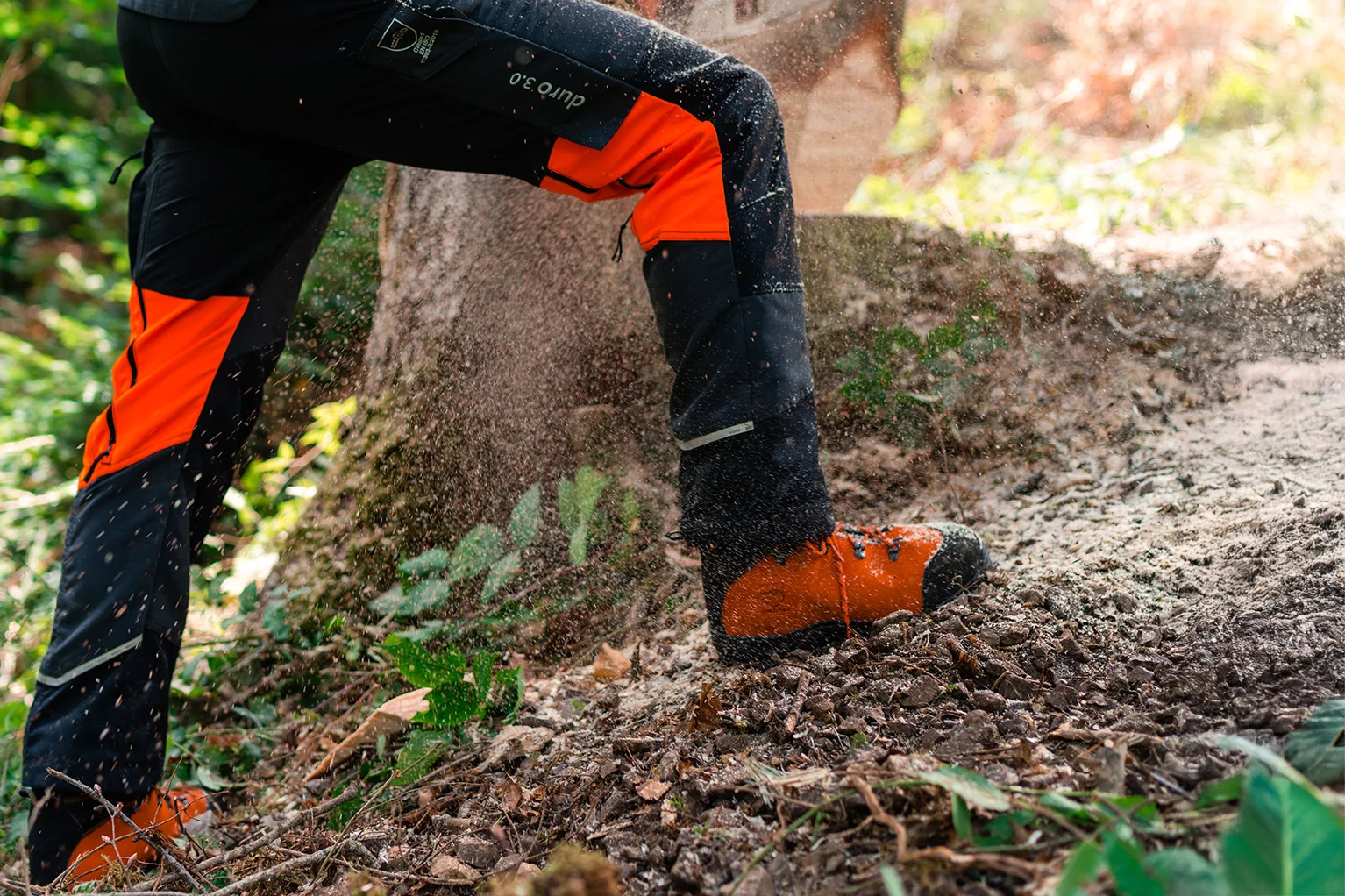 Beine einer Person mit Schnittschutzhose und Sicherheitsschuhen bei der Forstarbeit, Holzsp�ne fliegen.