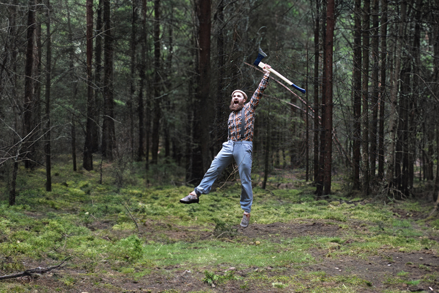 Mann mit Bart springt jubelnd im Forst in die Luft und hlt eine Axt mit blauem Kopf ber dem Kopf.